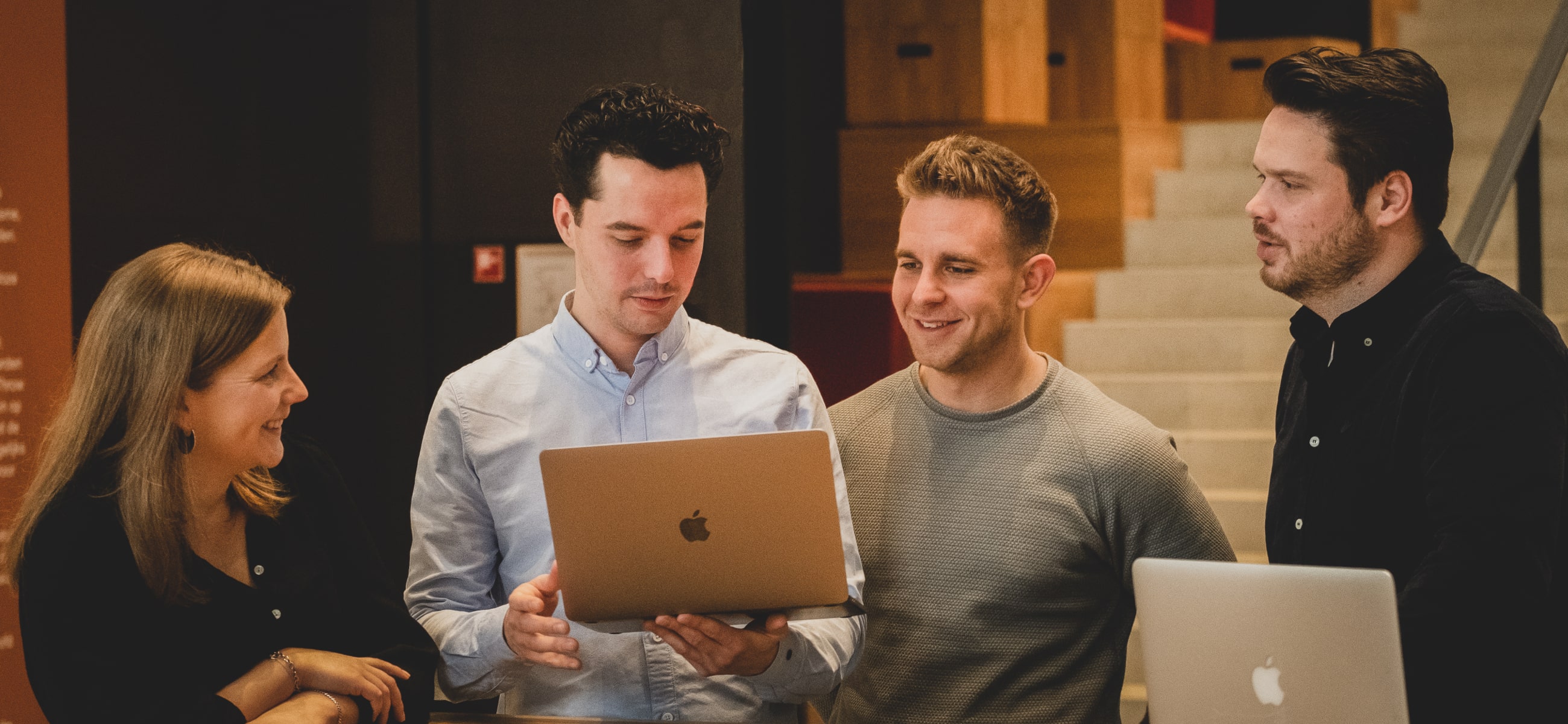 Een foto van Steven Oosterbeek, de oprichter van Stooseflow, die staat en omringd wordt door drie mensen die naar het scherm van zijn laptop kijken